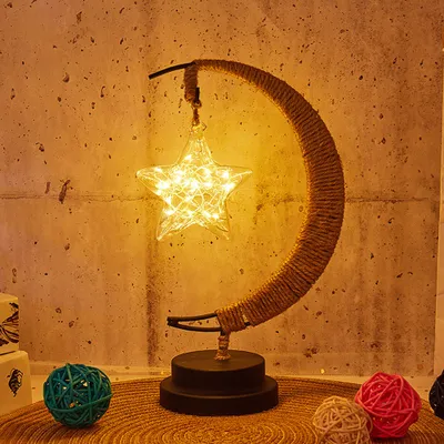 A decorative LED lamp shaped like a crescent moon with a star hanging from it, placed on a table with other decorative balls.