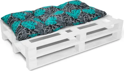 A cushion with a tropical leaf pattern is placed on a white wooden pallet.