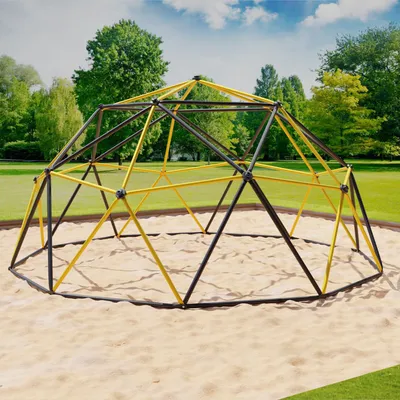 A geodesic dome climber playground structure in a park setting with sand on the ground and trees and sky in the background.