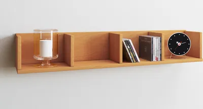 A wooden shelf mounted on a white wall, displaying decorative items and CDs.
