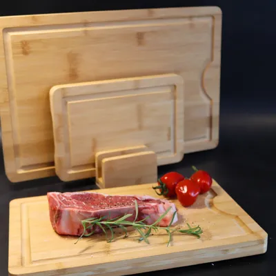A set of bamboo cutting boards with a raw steak and cherry tomatoes on the smallest board.