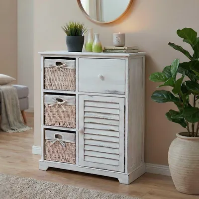 A white wooden chest of drawers with woven baskets and a louvered door, placed in a room with a plant and a mirror.
