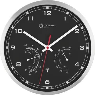 A close-up view of a wall clock with a black face, silver frame, and white hands. The clock face includes a thermometer and hygrometer.