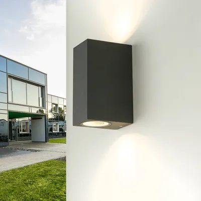 A modern building with glass windows and a grassy lawn, with a black outdoor wall light mounted on a white wall.