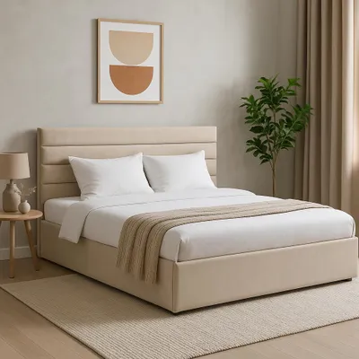 A bedroom scene featuring a bed with beige upholstery, white bedding, and a throw blanket. A framed abstract artwork hangs on the wall above the headboard, and a potted plant is visible to the right.