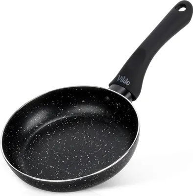 A black frying pan with a speckled interior and a black handle, shown from a diagonal angle against a white background.
