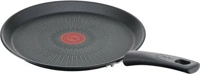 A close-up, angled view of a black frying pan with a red circular logo in the center.