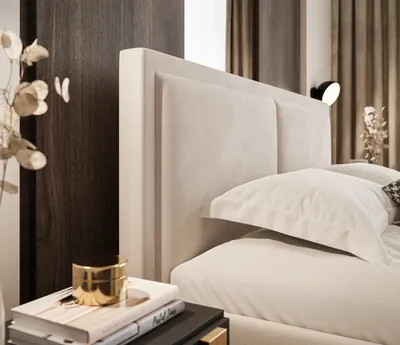 A close-up shot of a bed's headboard and bedding, with a bedside table in the foreground featuring books and a decorative jar.