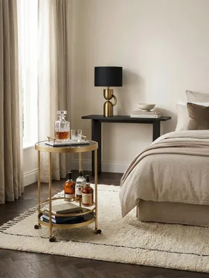 Eleganter Servierwagen in Gold und Schwarz, stilvoll in einem Altbau-Wohnzimmer mit Stuck und Parkettboden als mobile Minibar arrangiert._#sku_SAFWL6.000#