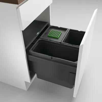 A pull-out kitchen waste bin system with multiple compartments, including a green divider, is shown extended from a white cabinet.