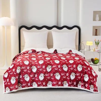 A Christmas-themed blanket with Santa Claus and gift patterns is laid out on a bed with white pillows.