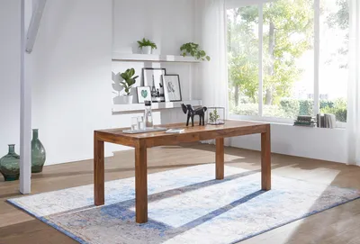 A dining room scene with a wooden table and chairs, set against a large window with natural light.