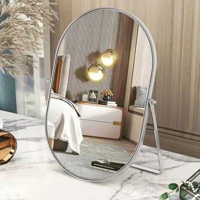 A vanity mirror is placed on a marble countertop in a bedroom setting, reflecting a bed and wall decor.