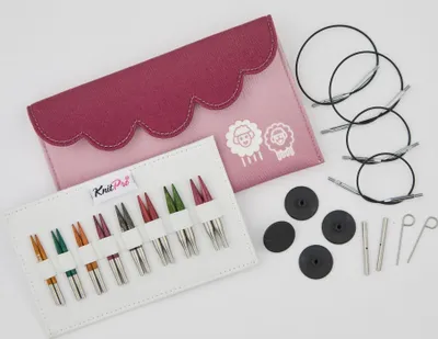 A flat lay of a knitting needle set, including a pink and purple case, various colored knitting needles, and circular knitting needles.