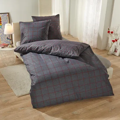 A neatly made bed with plaid bedding in a room with a lamp and curtains.