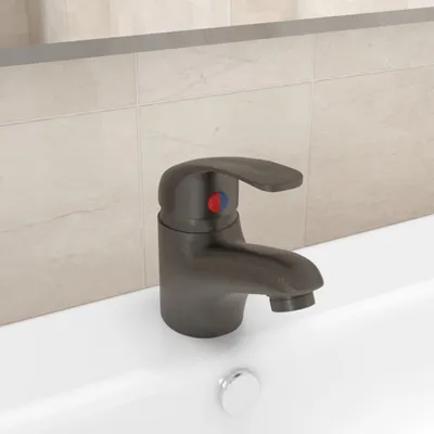 A close-up shot of a gray bathroom faucet with red and blue indicators for hot and cold water, positioned on a white sink. The background features light-colored tiles and a reflection in a mirror.