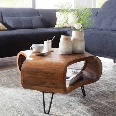 A wooden coffee table with a curved design, placed in a living room setting with a blue sofa and decorative vases.
