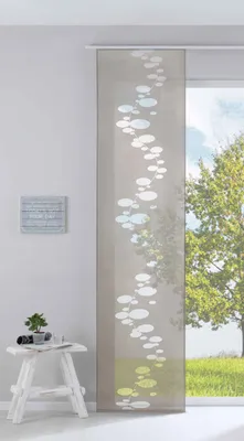 A panel curtain with a bubble pattern hanging in front of a window with a view of trees and grass.