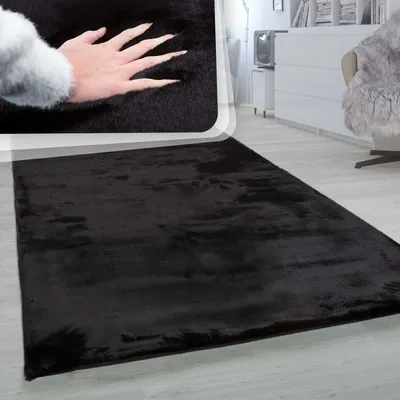 A close-up of a hand touching a black rug, with a wider shot of the rug on a floor in the background.