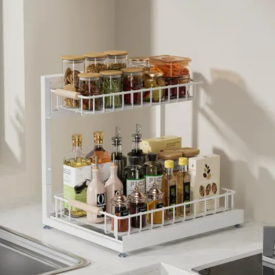 A two-tiered sliding kitchen organizer filled with various bottles of oils, vinegars, and spices, along with glass jars of spices and dry goods, is shown on a kitchen countertop.