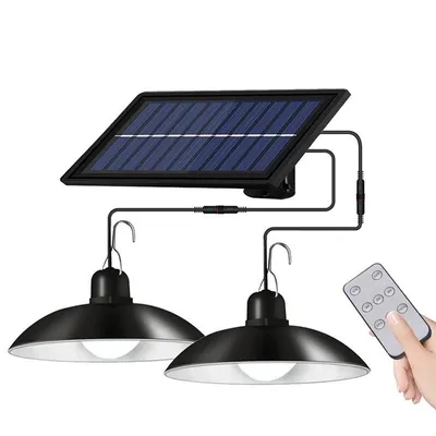 A solar panel connected to two pendant lights, with a remote control in a person's hand.