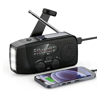 A black emergency radio with a solar panel, LED flashlight, and a smartphone connected to it for charging.
