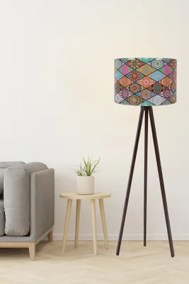 A floor lamp with a patterned lampshade stands next to a sofa and a small side table with a plant.