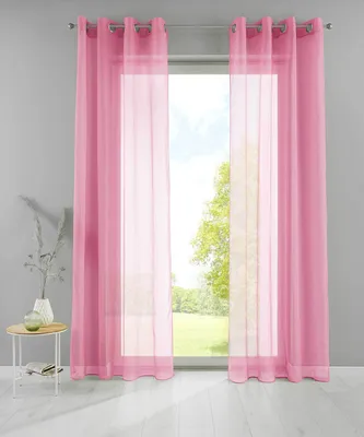 Two pink sheer curtains are hung on a window, with a view of trees and sky outside. A small round table with a vase and a book is placed to the left of the curtains.