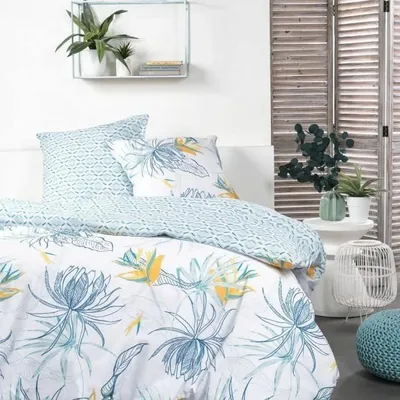 A bedroom setting with a bed dressed in a floral duvet cover and pillows, next to a wooden folding screen and decorative items.