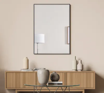 A mirror with a black frame is mounted on a light beige wall above a wooden console table with decorative vases and books.