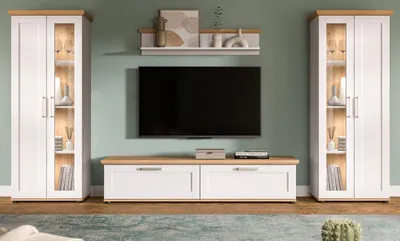 A living room scene featuring a TV entertainment unit with two tall cabinets and a media console, all in white and wood tones, against a light green wall.