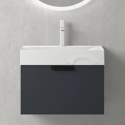 A modern bathroom vanity with a white sink and a dark gray drawer against a concrete wall.