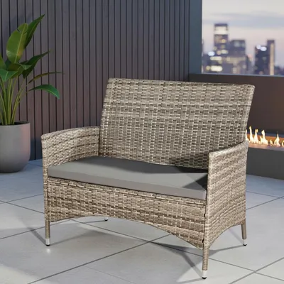 An outdoor seating area at dusk with a rattan bench and a fireplace.