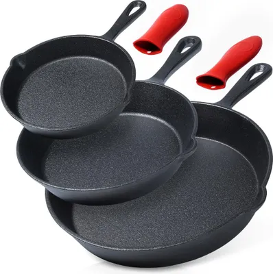 A set of three cast iron frying pans of varying sizes, stacked and arranged diagonally. Two red silicone handle covers are placed above the pans.