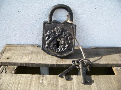 A vintage-style padlock with two keys rests on a wooden surface against a textured white wall.