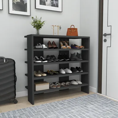 A dark gray shoe cabinet filled with various shoes and a small box, placed against a light gray wall with framed pictures above. A suitcase is visible to the left.