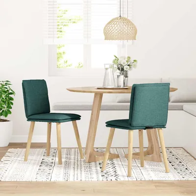 Two dark green fabric dining chairs are placed around a round wooden dining table in a bright, naturally lit room with a window and blinds.