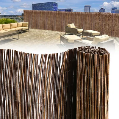 A rooftop patio with furniture and a bamboo fence, with a rolled-up bamboo fence in the foreground.
