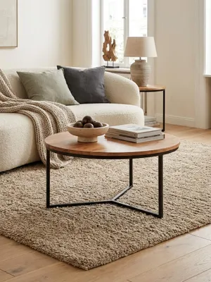 Eleganter runder Couchtisch aus Akazie Massivholz mit schwarzem Metallgestell in einem hellen, modernen Wohnzimmer, perfekt neben einem Sofa platziert._#sku_SAFWL6.368#