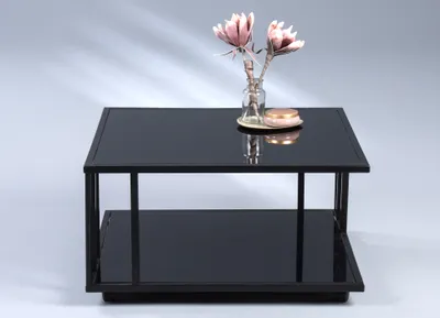 A black glass and metal coffee table with two shelves, decorated with a small vase of pink flowers and a round pink object.