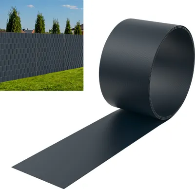 A roll of dark gray PVC privacy screening material is shown unrolling from the roll, with a section of a dark gray fence with a woven pattern in the background.