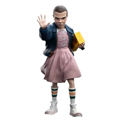 A figurine of Eleven from Stranger Things, holding a yellow box and raising her hand.