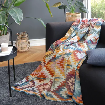 A colorful geometric patterned throw blanket draped over a dark sofa in a living room setting.
