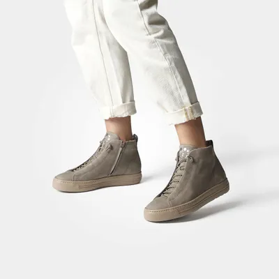 A person wearing white pants and grey high-top sneakers.