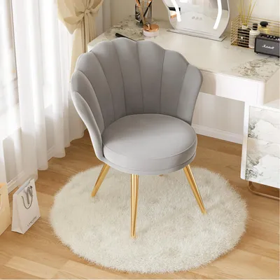 A gray upholstered chair with gold legs sits on a white fluffy rug in front of a vanity.