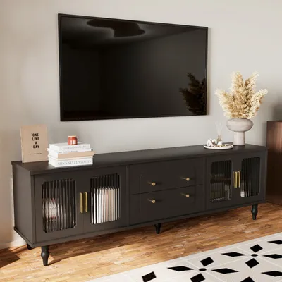 A black TV stand with glass doors and gold handles is shown against a light gray wall, with a large black TV mounted above it.