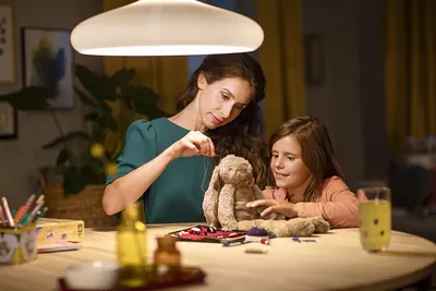 A mother and daughter are sewing a stuffed bunny together at a table.