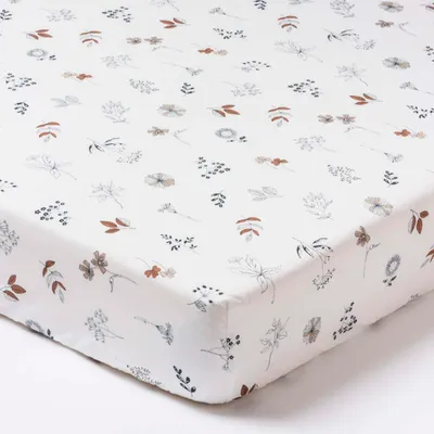 A close-up view of a white crib sheet with a floral pattern.