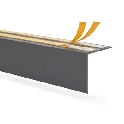A close-up, angled view of a dark gray corner profile with yellow adhesive tape being peeled off.