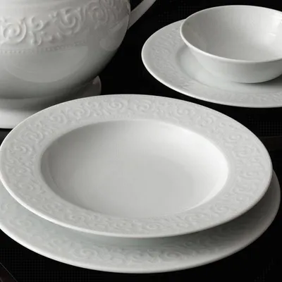 A close-up view of white porcelain dinnerware with ornate embossed patterns.
